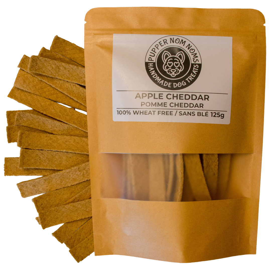 A stand-up pouch of Pupper Nom Nom Homemade Dog Treats, Apple Cheddar, shown with several rectangular cheddar treats fanned out to the left on a white background.